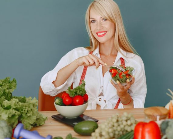 Blonde woman enjoying a fresh salad surrounded by vegetables, promoting healthy eating.